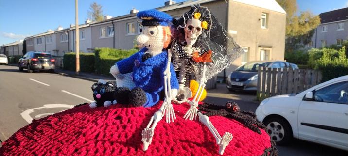 A knitted Postman Pat next to a model of a skeleton bride as part of a knitted installation on the top of a British post (pillar) box