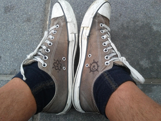 closeup of the feet of a person wearing old black Converse Chuck Taylor running shoes with white shoelaces... the shoes have turned grey with time and use... the left shoe has a smiling star doodle on it, and the right one has a smiling sun...