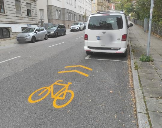 eine Sharrows Markierung führt direkt in ein geparktes Auto.