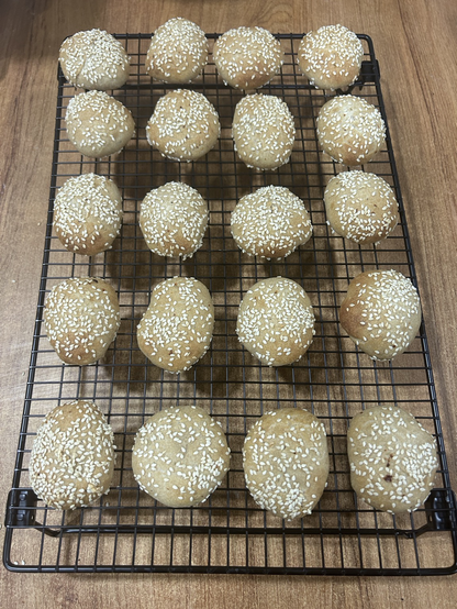 Closeup from above of 20 little bread rolls sitting on my new cooling rack, which is bigger than my formerly biggest one, and this one has foldable legs, which makes storage easier. The breads have a nice light bronze colour, which gives the sprinkled-on sesame seeds a festive air.