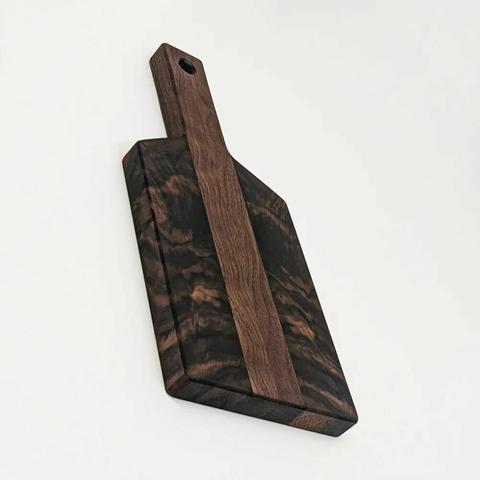 A walnut cutting board shaped like a paddle. The face has symmetrical grain patterns that are strikingly abstract.