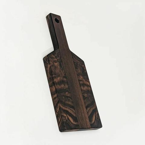 A walnut cutting board shaped like a paddle. The face has symmetrical grain patterns that are strikingly abstract.