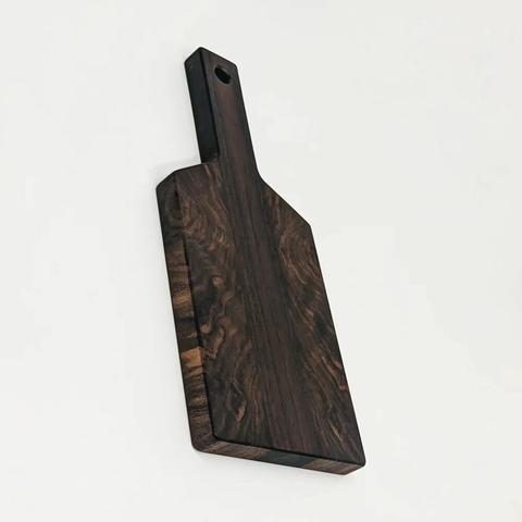 A walnut cutting board shaped like a paddle. The face has symmetrical grain patterns that are strikingly abstract.