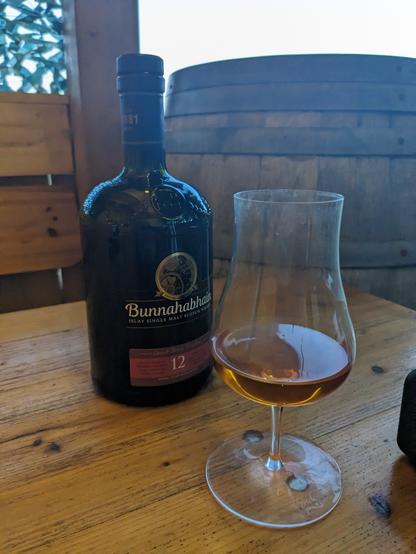 Bottle of Bunnahabhain 12 on a wooden table. A filled Glas next to it.
A wine barrel in the background