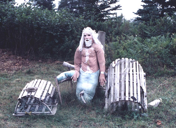 Bob Marchand photo of the Scarecrows of Necum Teuch, showing scarecrow of what looks like King Neptune of the sea, between two wooden lobster traps
