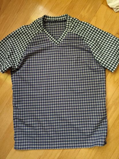 V-neck t-shirt in two small checked/plaid fabrics that are similar in design size, different in coloration. Blue and white checks form the sleeves and collar band while the body is blue and tan with a hint of a red stripe.