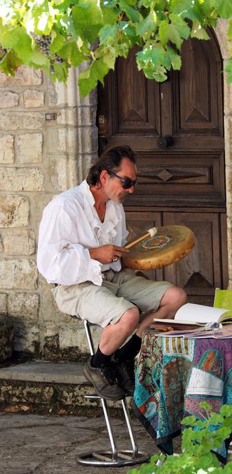 Dans un petit village de Lozère, devant une vieille porte en bois et sous une vigne grimpante, un chaman accompagne ses incantations au son d'un tambourin.
