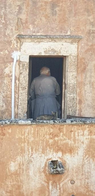 Religieux vu de dos au travers de la fenêtre d'un monastère, avec un chat sur la margelle, sur l'île de Crète en Grèce, photo prise en 2019