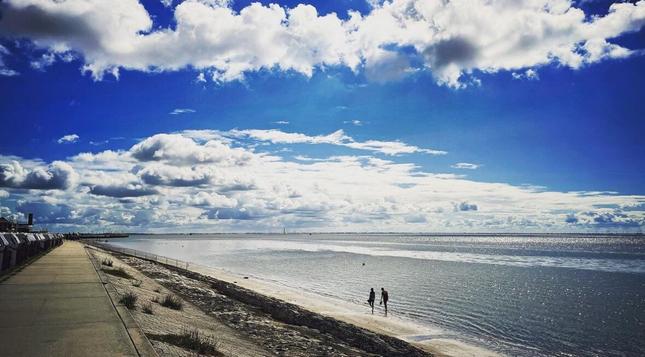 Wilhelmshaven‘s South Beach on a sunny day with a calm wadden sea and two people walking the beach in the distance.