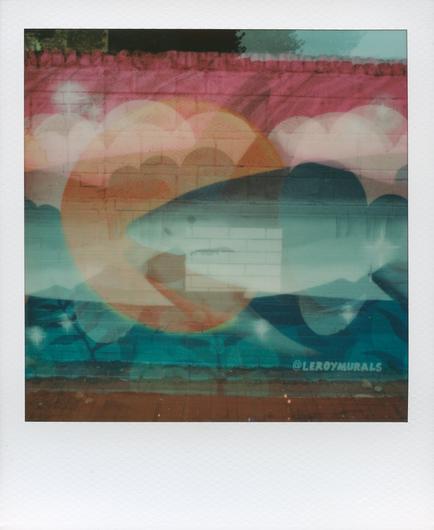 Colour multiple exposure polaroid of a Shark mural. Pink at the top changing to blue at the bottom. The head, body and tail are overlayed in the multiple exposure. The mural is painted on a brick wall.