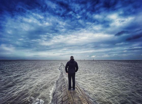 A man standing on a groyne watching the vastness of the North Sea surrounding him.