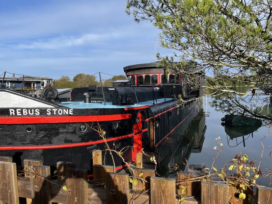A large barge converted into a house boat called “Rebus Stone”. The hull is black with bright red highlights. This was just about the only one out of 40 or so that looked seaworthy.