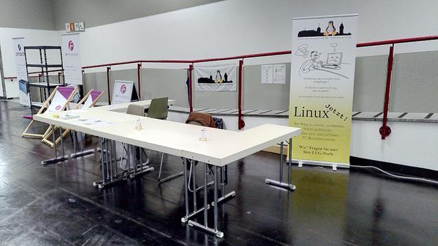 Unser Stand auf der Hack&Make 2023 auf Messe Nürnberg in der Halle 10 am Vorabend der Messe gegen 16:00 Uhr. Die Tische sind in einer U-Form angeordnet, rechts an der Wand steht unser Roll-Up mit dem Hinweis "Linux Jetzt!". Die Tische selbst sind noch leer und werden morgen früh vor Beginn der Messe mit unseren Materialien und Ausstellungsgegenständen bestückt.