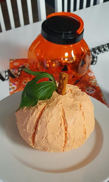 Ein Frischkäse in Kürbisform. Im Hintergrund eine Halloween-Leuchte und Deko.