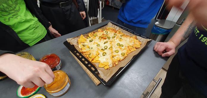 Ein Blech überbackener Nachos. Nerds stehen außenrum. Es gibt Dips dazu.