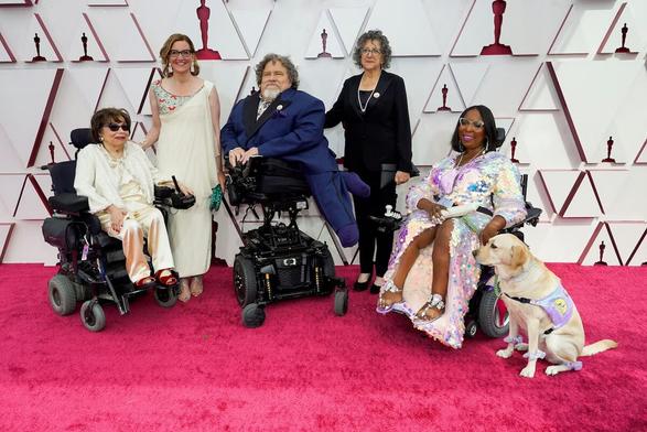 People from the documentary Crip Camp pose for photographers on the red carpet at the Oscars. From left: Judith Heumann, Nicole Newnham, James LeBrecht, Sara Bolder, Andraea LaVant, and service dog Gofi LaVant.