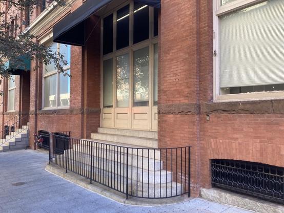 A wide set of stairs leading to a set of windows where doors probably were originally. There is also an awning covering the stairs. Despite leading to no where the stairs look perfect as seating but a railing has been placed around the steps so they aren’t accessible.