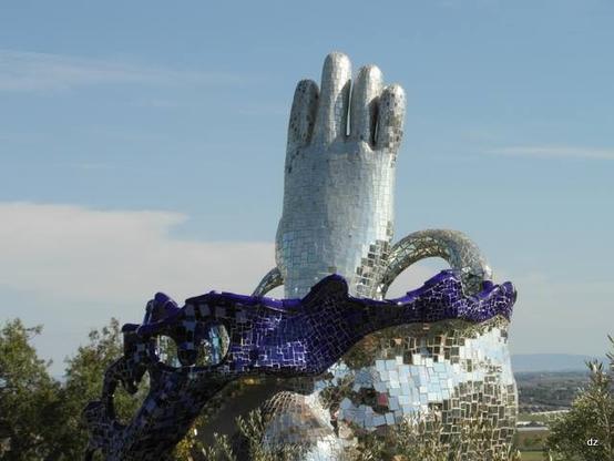 Ein riesiger Fuss mit vier Zehen ragt in den blauen Himmel. Das Fundament besteht aus blauen und verspiegelten Kacheln. Das Kunstwerk ist von Niki de Saint Phalle und steht in ihrem Tarot Garten in der Toskana.