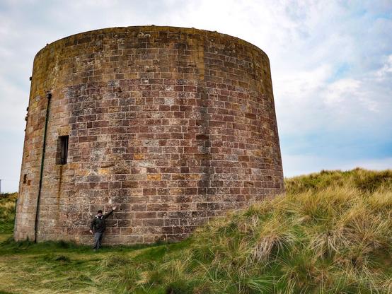 A Martello Tower with a person standing in front of it looking very small by comparison.
