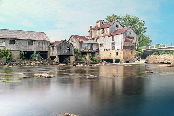 The historic Chishom Mill, in operation since the mid 1800s, sits by the glassy waters of a river on a beautiful sunny day in Chisholm, Ontario.