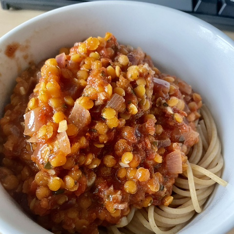 Close up picture of lentil bolognese on top of whole grain spaghetti in a while bowl.