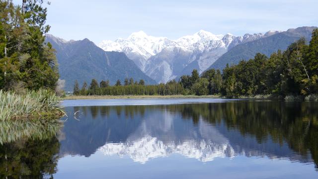 Horokoau/Mt Tasman & Aoraki/Mt Cook from  the Reflection Island Lookout at Lake Matheson. The lake reflects the mountains but the reflection is blurred by water movement caused by the breeze