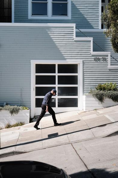 A man leaning forward while walking up a steep street.