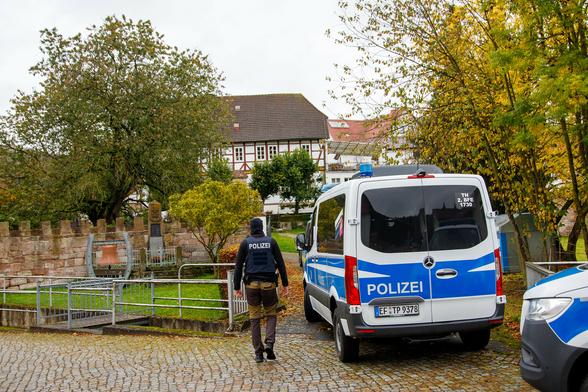 In Vordergrund ein Polizist vermummt von hinten neben einem BFE Polizei Fahrzeug, im Hintergrund das Haus von Thorsten Heise