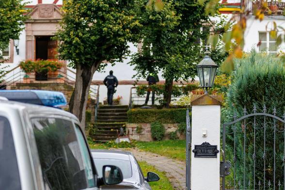Im Vordergrund links unscharf ein Polizeiauto, rechts ein Zaun und ein Klingelschild mit "Heise", im Hintergrund das Haus von Thorsten Heise. Im Aufgang zum Eingang steht ein Polizist