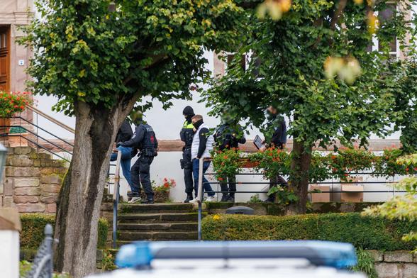 Neonazi Gianluca Bruno geht vermummt mit mehreren Polizisten in die Richtung des Eingans von Thorsten Heises Anwesen. Rechts stehen Umzungskartons mit sichergestellten Sachen