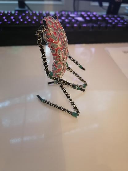 Man sieht ein Foto von Metalldraht, Alufolie und Tape, das so zusammengeformt wurde, dass es einer knieenden Figur ähnelt. Auf ein solches "Skelett" kommt im nächsten Schritt die Modelliermasse. Die Figur hat noch keinen Kopf.