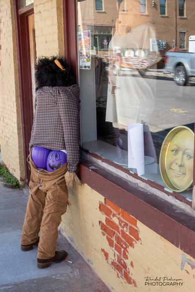 Full size figure leans against wall with pants partially down exposing buttocks made of 2 purple plastic pumpkins.