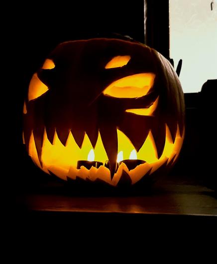 A scary Halloween pumpkin sitting on a countertop with fire-red light emanating from it. It has a big sharp-toothed grin and gleeful eyes. It appears to be laughing malevolently.