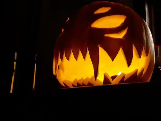 A scary Halloween pumpkin sitting on a countertop with fire-red light emanating from it. It has a big sharp-toothed grin and gleeful eyes. It appears to be laughing malevolently.