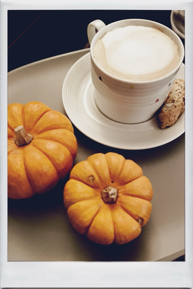Two small pumpkins, A cappuccino in a Porcelain cup with a biscotti on the saucer.. A stiil life in warm light.