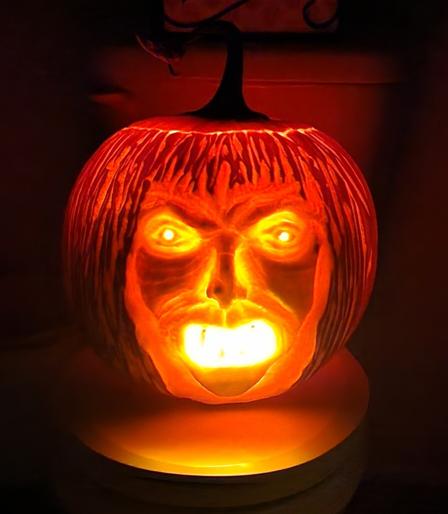 Carved Halloween face in a pumpkin.  Resembles an angry old woman/witch with straggly hair. It's now dark and the light inside male it glow.