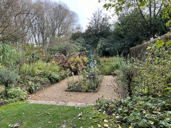 Tuin met groenig kunstwerk in het midden met gravelvierkant er omheen.