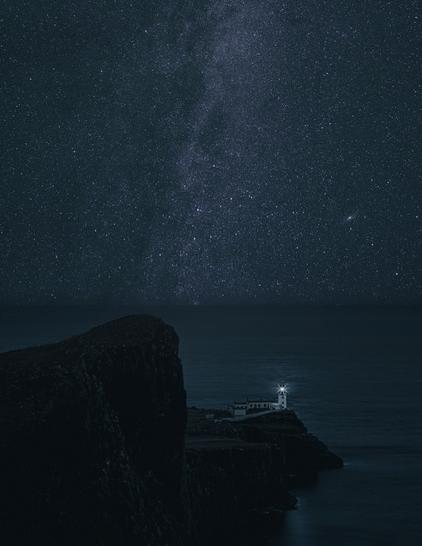 Picture of Neist Point on Isle of Sky. On a prominent lance a lighthouse spreads its light. In the background is the Milky Way in the night sky.