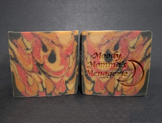 A red, orange, yellow and black soap that looks like fire. The right bar is stamped with a crescent moon and "Moody Momma's Menagerie"