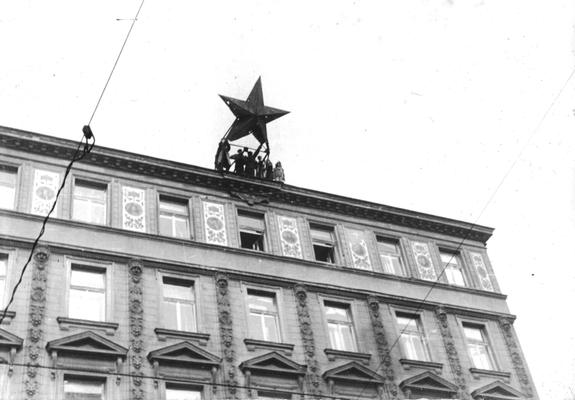 A group of people are on the edge of the floor on a large building dismantling a large star-shaped sign.