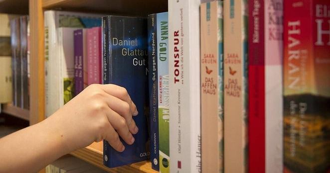 photo of hand holding a book among other books on a shelf