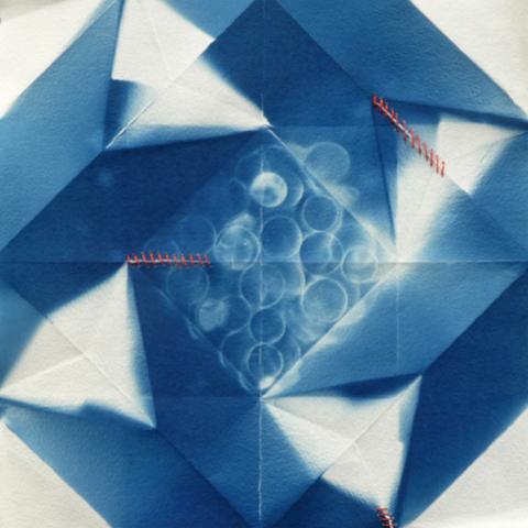 Imagine an origami bowl, 4 sided, folded from a single sheet. Unfolded, the areas where light touched the bowl are now blue. The areas of the paper which were hidden from light are white. The square central area has negative images of circular forms, like ghost coins haunting the bowl. Running orizontally left from the centre, and diagonally halfway to the top right corner, are two short sections of simple red silk stitching.