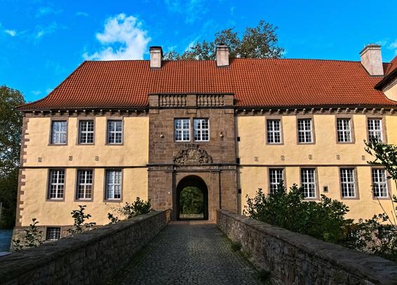 The south wing of the castle with an early Baroque gateway from the 17th century. The round arch portal is crowned by the coat of arms of the von Strünkede family. A stone bridge leads to the entrance.