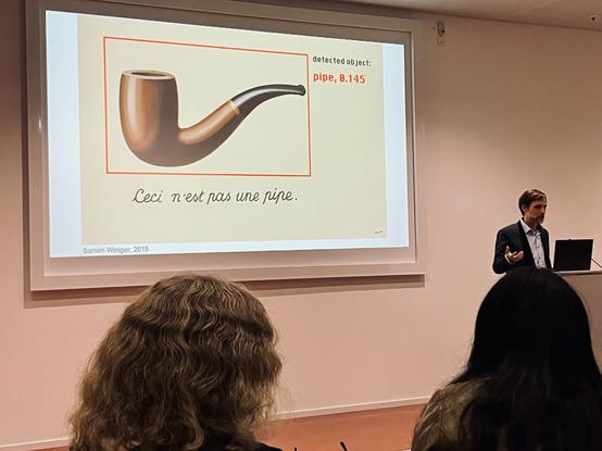 Folie zeigt Abbildung von René Magrittes „Ceci n’est pas une pipe“ und daneben das Ergebnis einer KI-Bilderkennung: 'detected object: pipe, 0.145'