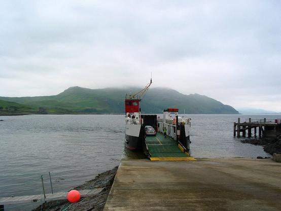 The small ferry at Kilchoan pier is preparing for the return trip to Tobermory on the Isle of Mull, which is clearly visible in the background with some clouds covering the top of the mountains