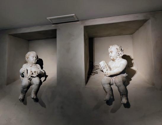 A photograph of two cherub statues, one hiding a skull and the other holding an hourglass.