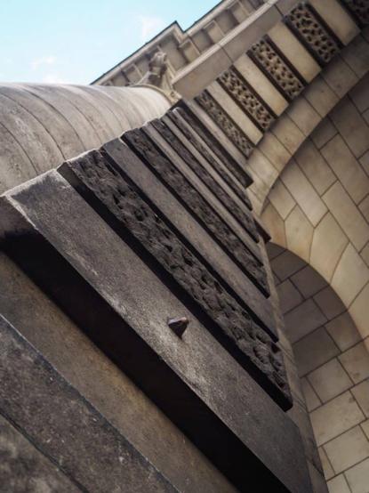 A view looking up at the inside of a stone archway, where a sculpted nose is protruding