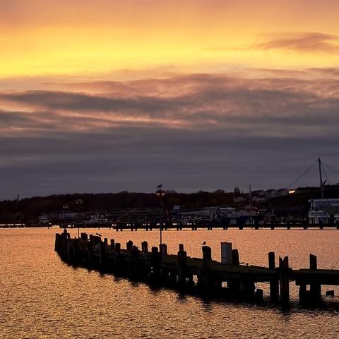 Die Ostsee im Hafenbecken spiegelt die goldene Farbe des Himmels.