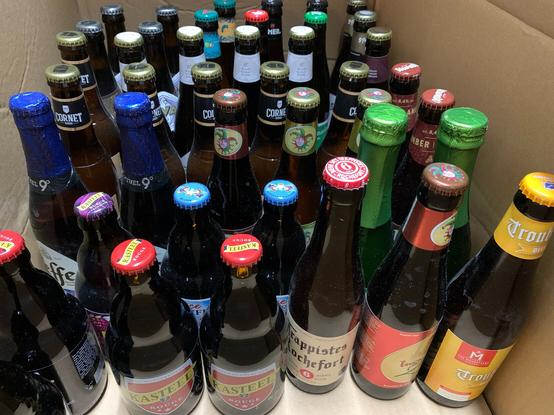 A cardboard box filled with a variety of bottled Belgian beers.
