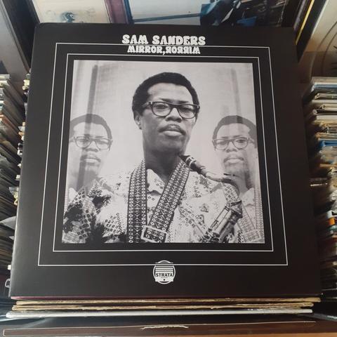 Album cover features a photo of Sam Sanders. He's wearing eyeglasses and has a saxophone in his hands, and a wide strap for the saxophone around his neck.